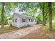 Single-story home with light blue siding, dark shutters, and a quaint front porch nestled among mature trees at 104 Willetta Dr, Charlotte, NC 28217