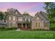 Beautiful stone home showcasing manicured lawn, colorful flower beds, and a charming walkway under a pink and purple sunset at 320 Eden Hollow Ln, Weddington, NC 28104