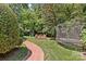 Landscaped backyard featuring a brick walkway, trampoline, playset, and lush greenery at 1200 Rutledge Ave, Charlotte, NC 28211