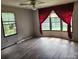 Bright living room with wood-look floors, ceiling fan, and large windows with red curtains at 269 Saddle Rd, Lancaster, SC 29720