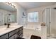 A bright bathroom featuring a soaking tub under a window, a glass-enclosed shower, and a dark vanity with double sinks at 1140 Landsdown Dr, Salisbury, NC 28147