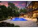Spacious backyard featuring a pool, spa, outdoor kitchen and fire pits against a backdrop of trees at twilight at 2288 Brawley School Rd, Mooresville, NC 28117
