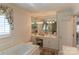 Bright bathroom featuring a soaking tub, vanity with makeup area, large mirror, and a window with floral curtains at 3008 Imperial Dr, Gastonia, NC 28054