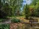 Secluded backyard with bench, a brick house with a lush, green landscape, and towering trees at 6001 Charing Pl, Charlotte, NC 28211