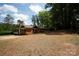 Rear exterior featuring a brick home, a gravel driveway and additional structures in a lush, wooded environment at 5100 Crestland Ave, Charlotte, NC 28269