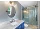 Bright bathroom featuring blue herringbone tile shower, round mirror, and vanity with marble countertop at 15333 Catawba S Cir, Matthews, NC 28104