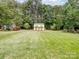 Expansive backyard with lush green grass, mature trees, and a storage shed at 7627 Woodcrest Dr, Stanley, NC 28164