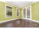 Bright room featuring hardwood floors, green walls, white trim, two windows with blinds, and glass french doors at 15536 Oleander Dr # L228, Charlotte, NC 28278