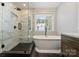 Bright bathroom featuring a modern bathtub, a tiled shower, and a window with a wooded view at 7833 Taymouth Ln, Charlotte, NC 28269