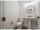 Bright powder room with stylish pedestal sink, round mirror, modern lighting, and a dark wood-look floor at 26056 Neptunes Lndg, Fort Mill, SC 29708