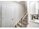 Carpeted stairway with wooden handrail and black iron balusters adjacent to a white door and white kitchen cabinets at 3844 Cheyney Park Dr, Charlotte, NC 28269