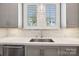 Close-up of the kitchen sink with gray cabinets, marble backsplash, stainless steel dishwasher, and white countertops at 7908 Rea View Ct, Charlotte, NC 28226