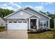 Charming gray home featuring a two-car garage, stone accents, manicured lawn and covered front porch entrance at 107 S Sina St, Troutman, NC 28166
