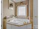 This is a bathroom featuring a soaking tub with gold fixtures and a lattice-patterned window at 400 Maymont Dr, Cramerton, NC 28032