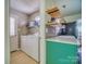 View of the kitchen, with green cabinetry and floating wood shelves, adjacent to a well-lit laundry room at 7122 Marlin St, Gastonia, NC 28056