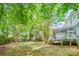 A spacious backyard with lush green grass, mature trees, play set, a wooden fence, and a charming deck and porch at 8709 Huntland Ct, Charlotte, NC 28277