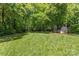 Large grassy backyard with a shed and a wooded area in the background, enclosed by a chain link fence at 1241 Rollins Ave, Charlotte, NC 28205
