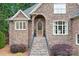 Stone steps lead to an arched entryway with a decorative door, complemented by manicured shrubs and brick accents at 7738 Burning Ridge Dr, Stanley, NC 28164