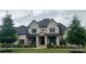 Elegant gray brick home with a covered front porch, black shutters, and lush landscaping creates curb appeal at 1152 Grand Oak Dr, Waxhaw, NC 28173