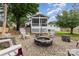 Landscaped backyard featuring a fire pit with chairs, a screened porch, and mature trees under a partly cloudy sky at 127 Leonidas St, Fort Mill, SC 29715