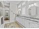 Spacious bathroom featuring double sinks, granite countertops, white cabinetry, decorative mirrors, and shuttered windows at 9750 Briarwick Ln, Charlotte, NC 28277