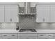 Close-up of modern gas cooktop with gray tiled backsplash and white cabinetry at 9750 Briarwick Ln, Charlotte, NC 28277