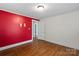 Bedroom with hardwood floors, neutral wall, and bright red accent wall at 24515 Saint Martin Rd, Albemarle, NC 28001