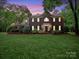 Beautiful brick two-story home with a well-manicured lawn and mature trees during dusk at 8527 Foxbridge Dr, Matthews, NC 28104
