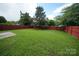 Green backyard with a well-maintained lawn, mature trees and red fencing at 4037 Lakota Ct, Charlotte, NC 28269