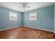 A brightly lit bedroom featuring hardwood floors, two windows, ceiling fan, and light blue painted walls at 800 Old Little Rock Rd, Charlotte, NC 28214