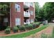 Exterior angle view of the brick apartment building with white balconies and manicured landscaping at 1000 E Woodlawn Rd # 107, Charlotte, NC 28209