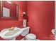 Compact red half bathroom featuring a pedestal sink, toilet, and decorative mirror at 1120 N College St, Mount Pleasant, NC 28124