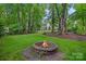 Scenic backyard featuring a stone fire pit surrounded by lush greenery and mature trees for a tranquil ambiance at 1402 Coachman Dr, Waxhaw, NC 28173