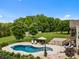 A kidney-shaped pool is surrounded by patio furniture in this backyard with trees and greenery, basketball court and shed at 1115 Wynnbrook Way, Concord, NC 28027