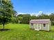 A green and brown shed sits on a large, grassy lot with a tree in the foreground at 1115 Wynnbrook Way, Concord, NC 28027