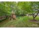 Spacious backyard featuring a playground, a shed, and bordered by a wooden fence and lush trees at 144 Chickasaw Dr, Shelby, NC 28152