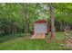 Exterior view of a red shed with a ramp and roll up door, nestled among trees on a grassy lawn at 144 Chickasaw Dr, Shelby, NC 28152