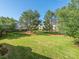 Expansive backyard featuring lush green grass, mature trees, and a building in the background at 8747 Coralbell Ln, Charlotte, NC 28213