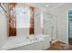 Well-lit bathroom features a soaking tub, a glass shower, and a chandelier hanging by the window at 43041 Mimosa Ct, Fort Mill, SC 29707