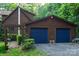 Exterior of a log home featuring a two-car garage with blue doors and surrounding lush landscaping at 95 Odell Ct, Taylorsville, NC 28681