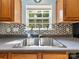 Close-up of the kitchen sink under a window, accented by a tiled backsplash and wooden cabinets at 3446 Broadwick St, Charlotte, NC 28213