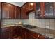 Close-up of a kitchen with granite countertops, stainless steel gas cooktop, and dark wood cabinetry at 8914 Landsdowne Ave, Harrisburg, NC 28075