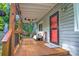 Inviting covered porch featuring wood decking, railing, seating, and a vibrant red front door at 5995 Tall Tree Ln, Harrisburg, NC 28075