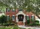 Traditional red brick home with a covered entrance, an American flag, and established shrubs at 8612 Tintinhull Ln, Waxhaw, NC 28173