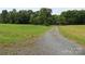 Gravel road leading through a large grassy field, surrounded by mature trees, creating a private setting at 344 Lucas Rd, Star, NC 27356