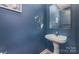 Stylish powder room with a pedestal sink, decorative mirror, and dark blue accent wall at 8927 Comstock Ct, Locust, NC 28097