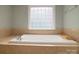 A luxurious soaking tub in a bright bathroom with tile surround and a frosted window at 9913 Hazelview Dr, Charlotte, NC 28277