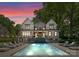 Twilight view of a backyard pool, stone exterior, and outdoor seating area with landscape lighting at 1550 Queens W Rd, Charlotte, NC 28207