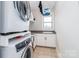 Bright laundry room features tiled flooring, window with sink and stacked washer and dryer at 324 Squash Harvest Ct, Matthews, NC 28104