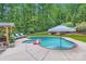 Backyard pool and hot tub surrounded by mature trees with outdoor furniture and an umbrella at 1056 James Madison Dr, Matthews, NC 28104